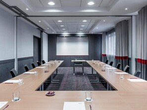 Un salón de conferencias con una larga mesa, sillas, una pantalla de proyector y piso alfombrado.