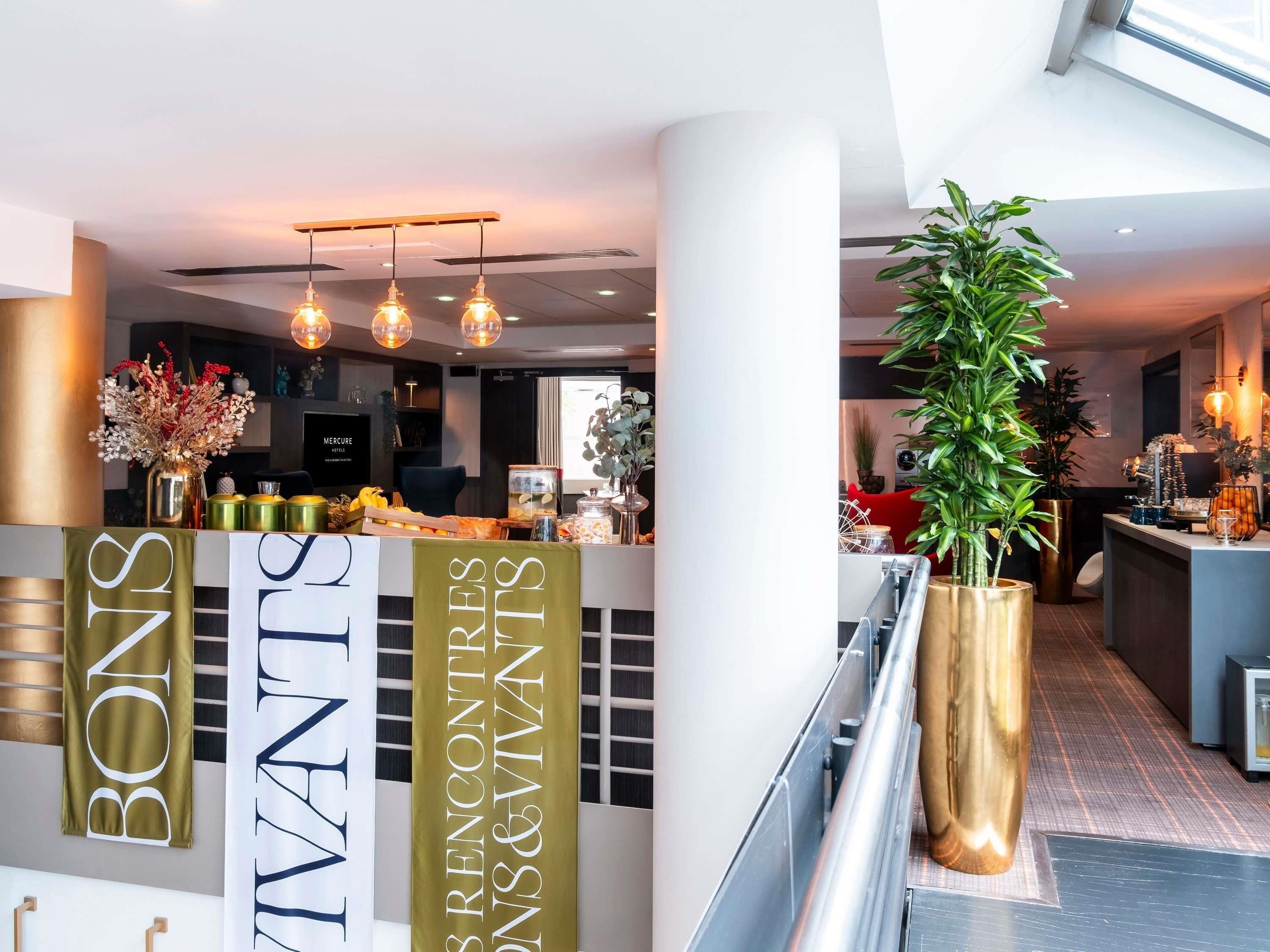 Een moderne hotel lobby met een receptiebalie, een grote kamerplant en een spandoek met de naam van het hotel.