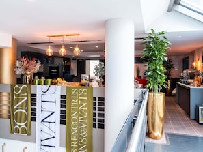 A modern hotel lobby with a reception desk, a large potted plant, and a banner with the hotel's name. - Mercure Paris La Défense Grande Arche (Nanterre)