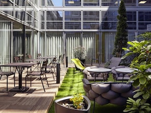 A modern outdoor patio with a wooden deck, metal furniture, and a small artificial turf area. - Mercure Paris La Défense Grande Arche (Nanterre)