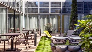 A modern outdoor patio with a dining area, seating, and a small garden. - Mercure Paris La Défense Grande Arche (Nanterre)