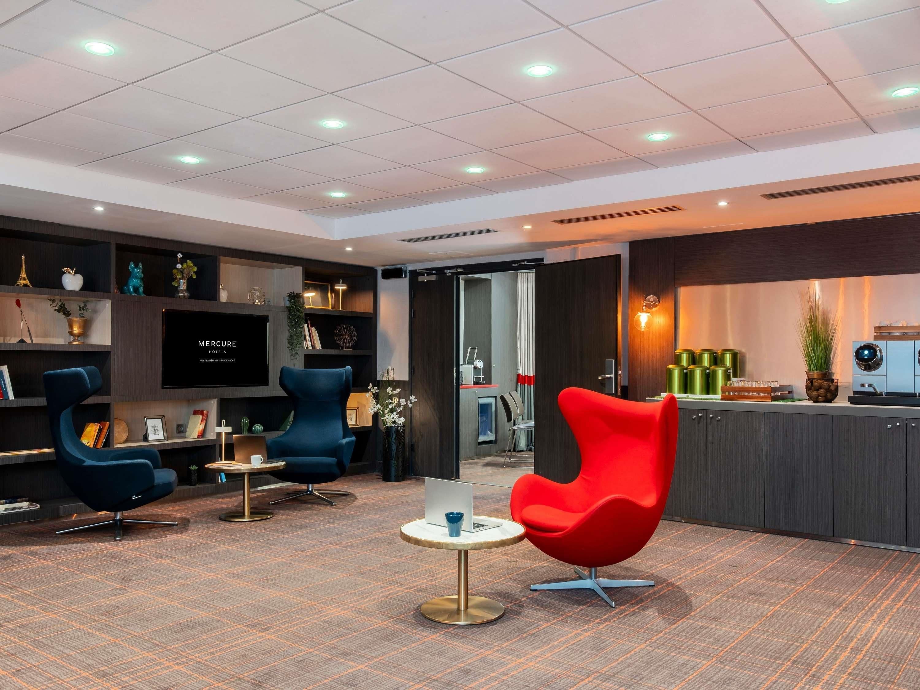Een moderne hotellobby met een zithoek, een bar en een televisie waarop 'MERCURE HOTELS' staat.