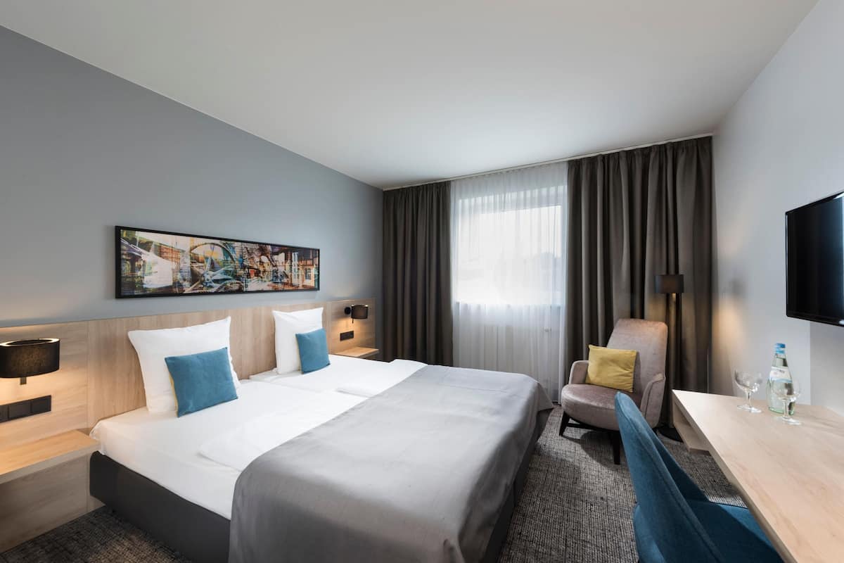 Habitación de hotel con una cama grande, un escritorio, una silla, un televisor de pantalla plana y un cuadro en la pared.