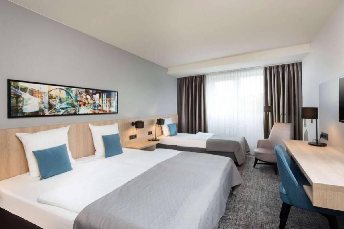 Habitación de hotel con dos camas, un escritorio, una silla, un televisor y un cuadro abstracto grande en la pared.