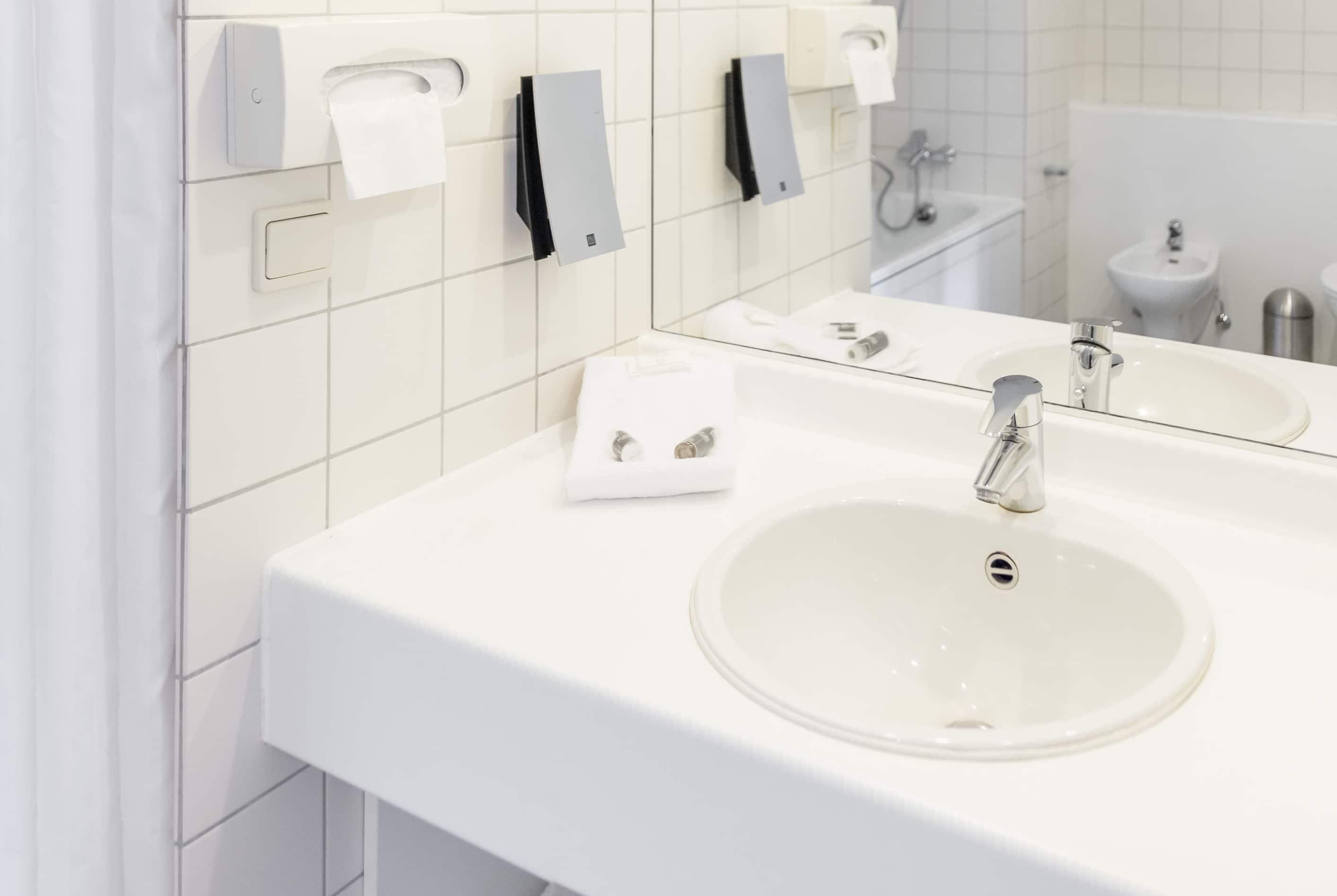 Un baño moderno con un lavamanos blanco, un espejo y dispensadores de toallas.
