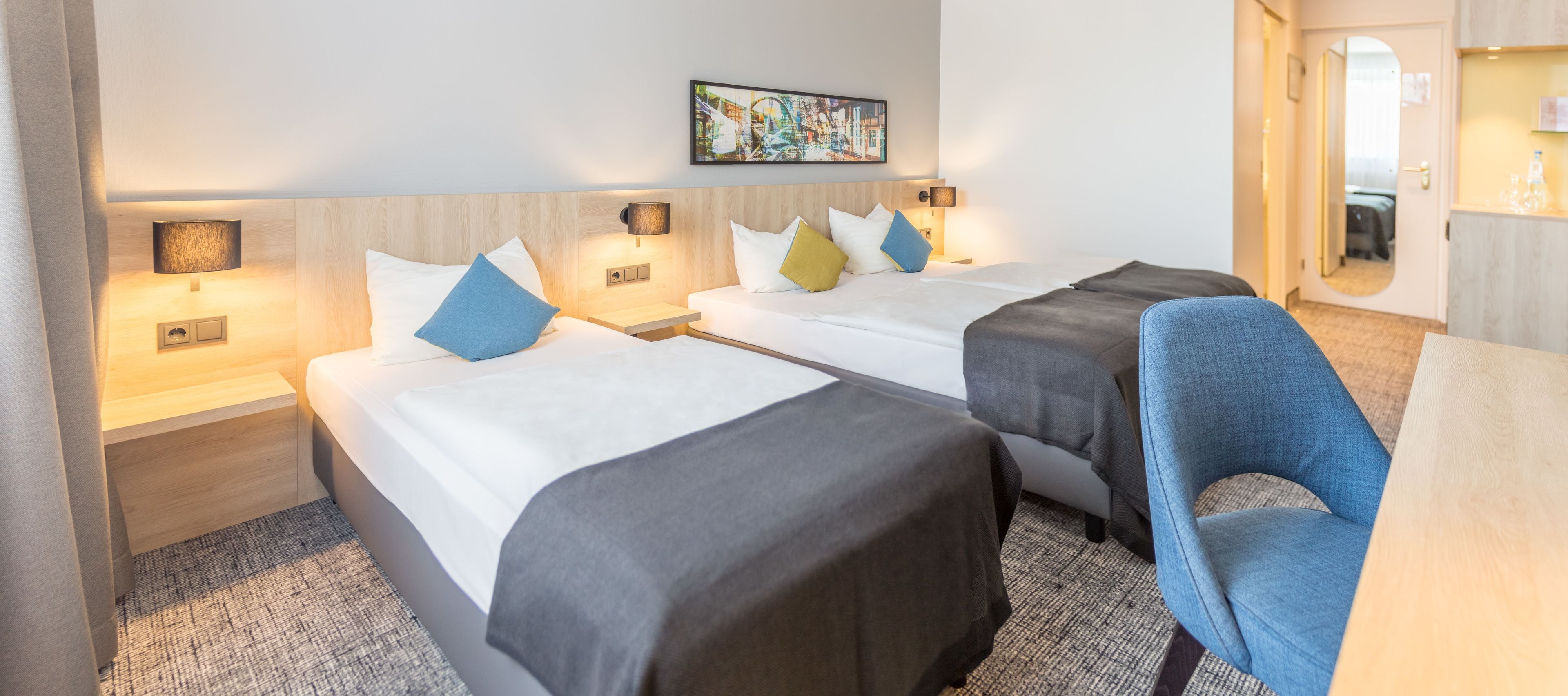 Et hotelværelse med to senge, et skrivebord, en stol og et stort spejl.