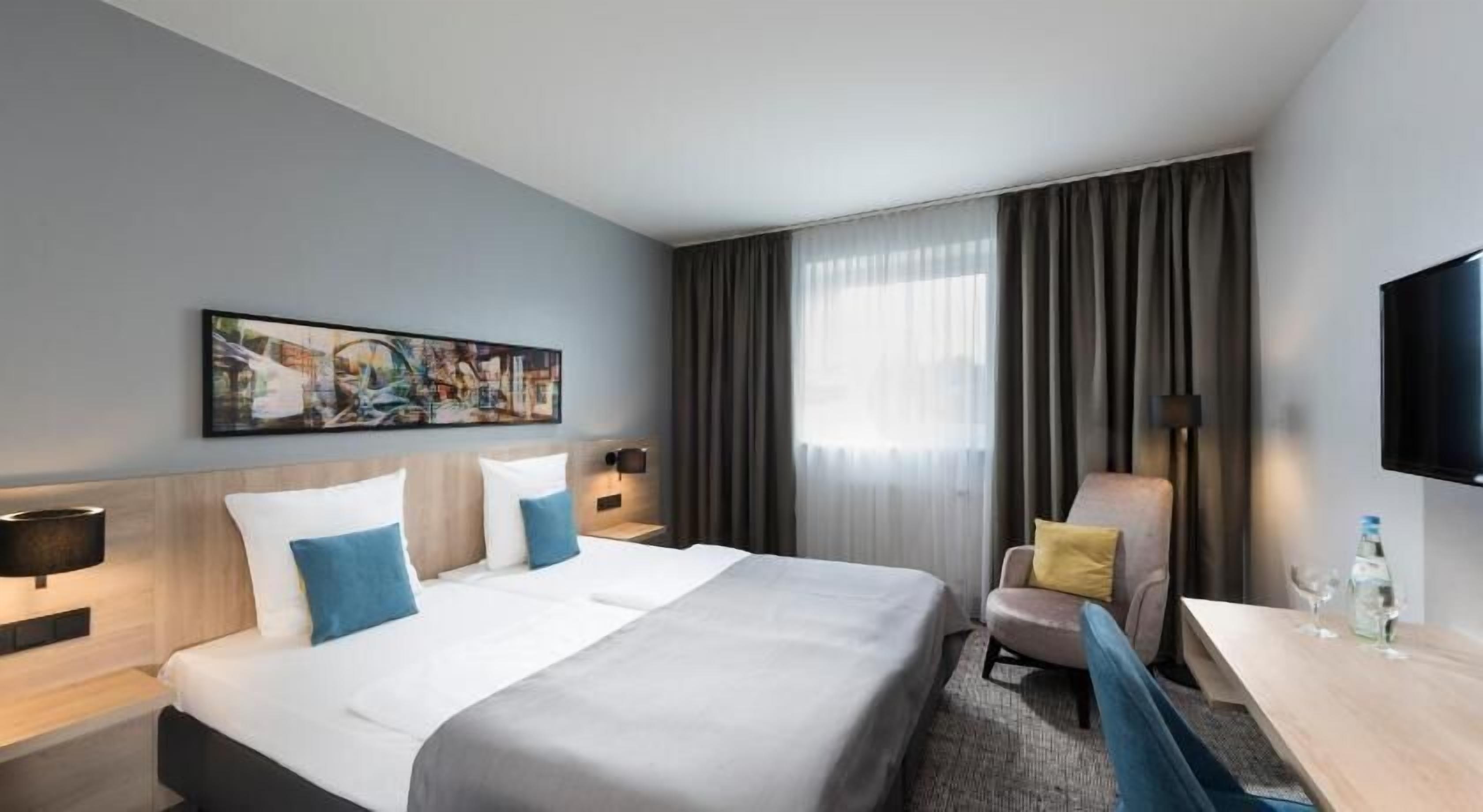 Habitación de hotel con cama, escritorio, silla, televisor y un cuadro en la pared.