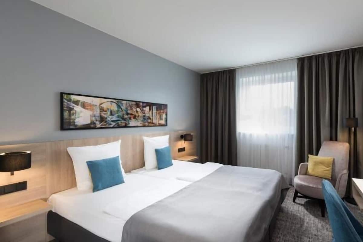 A hotel room with a bed, a desk, a chair, a television, and a painting on the wall.