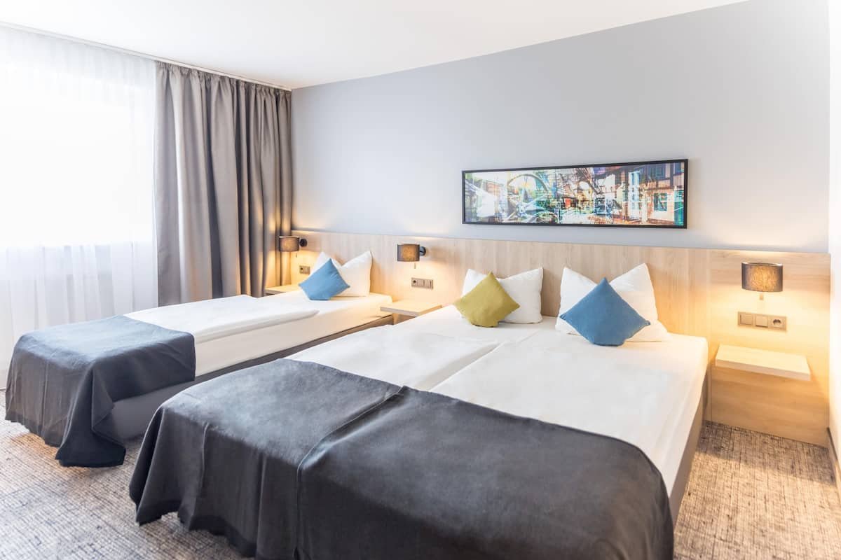 Habitación de hotel con dos camas, un ventanal con cortinas, un cuadro en la pared y lámparas de noche.
