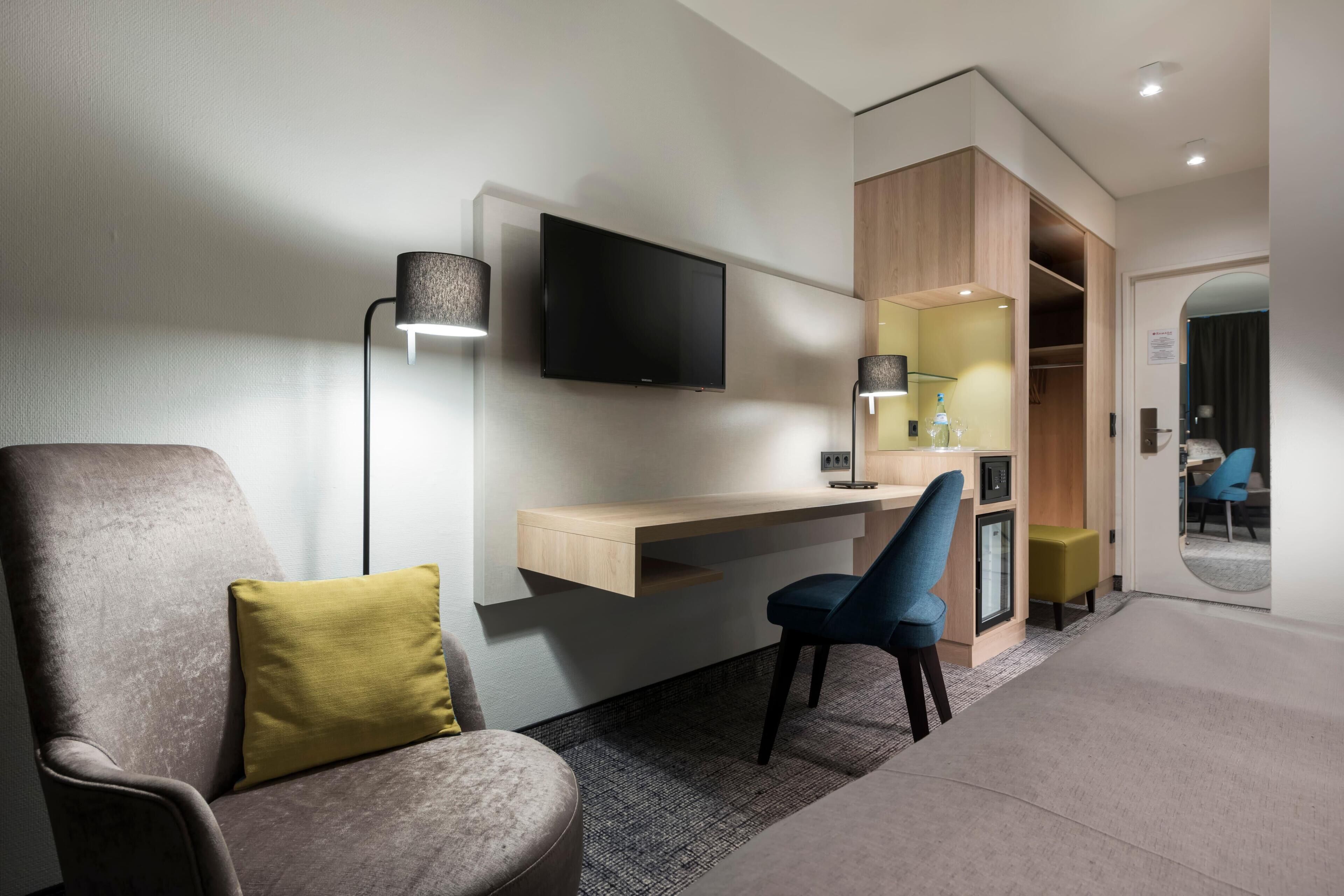 Une chambre d’hôtel moderne équipée d’un bureau, d’une chaise, d’une télévision et d’une armoire.