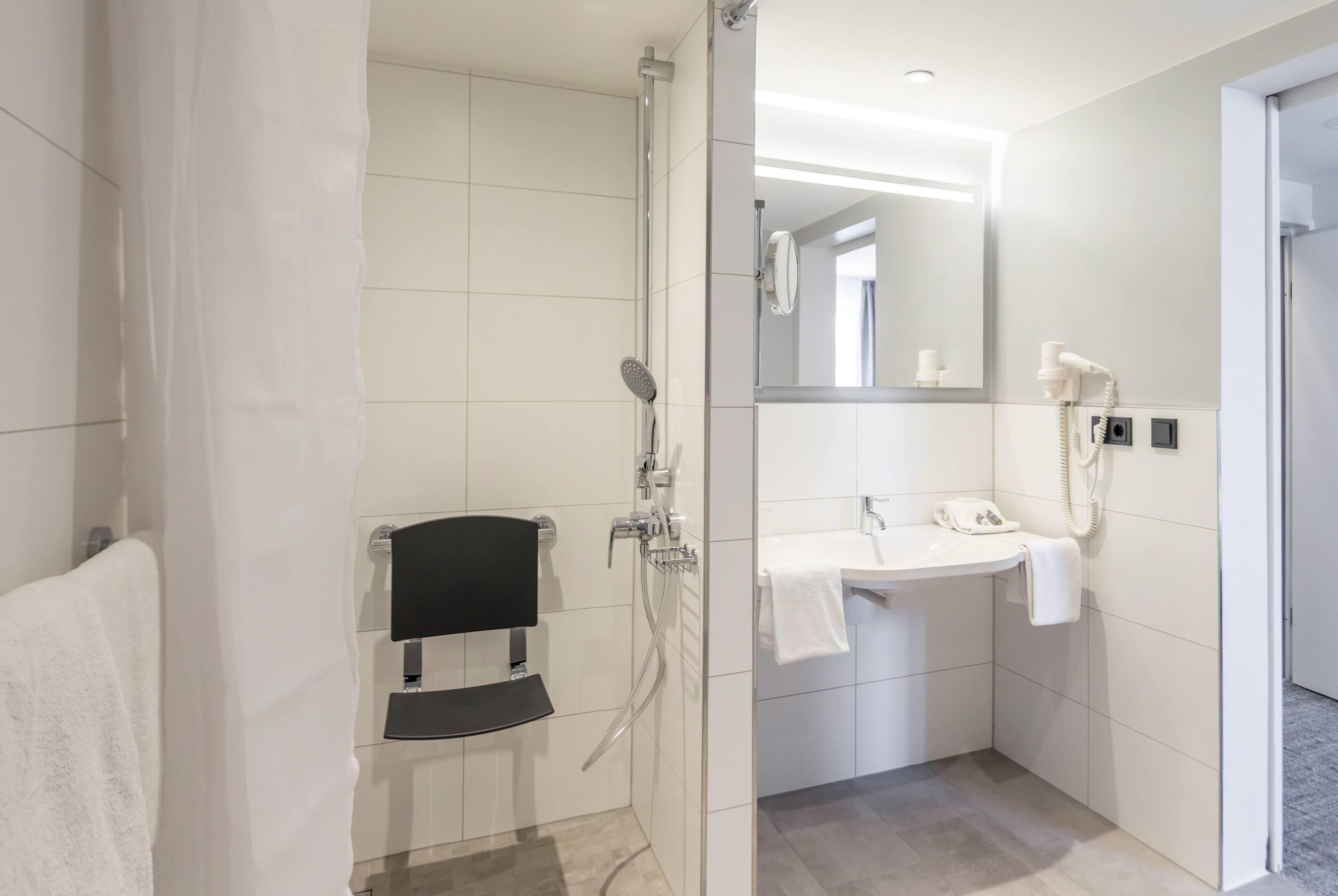 A modern bathroom with a shower, a sink, a mirror, and a towel rack.