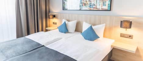 Habitación de hotel con una cama grande, dos mesitas de noche con lámparas, una obra de arte en la pared y vistas a un paisaje urbano.