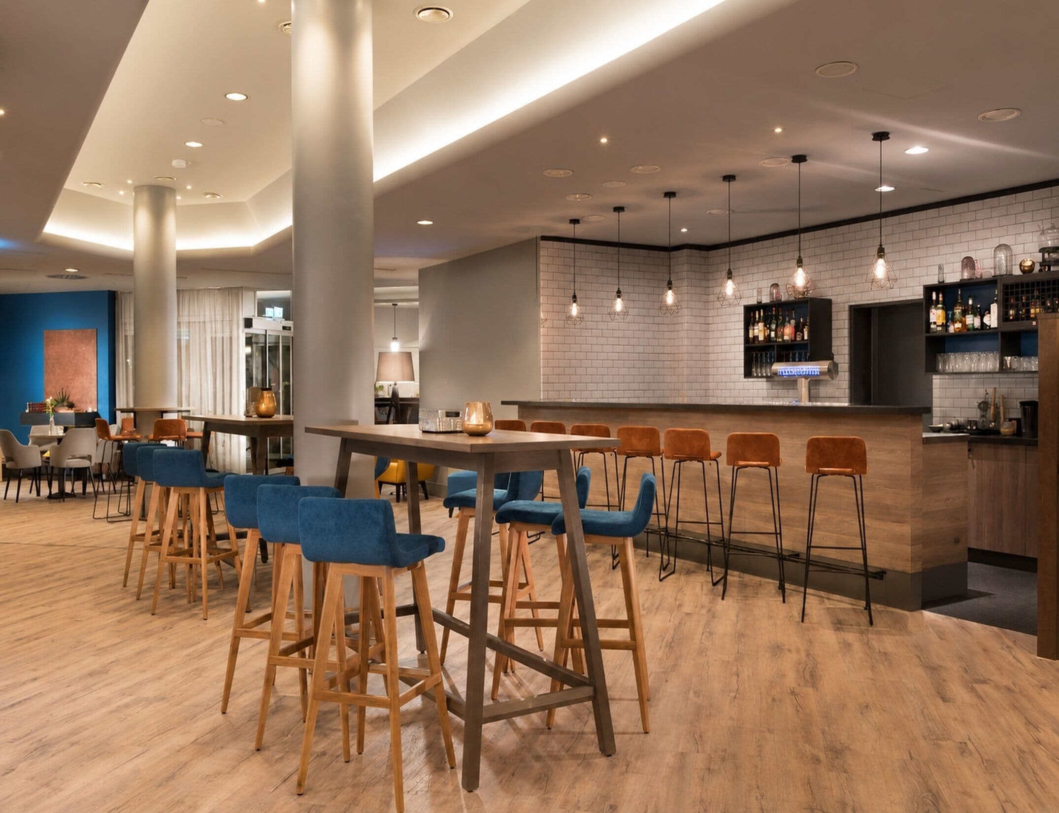 Eine moderne Bar mit Holzhockern, einer Theke und hängenden Pendelleuchten.
