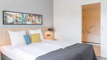 A hotel room with a bed, a nightstand, a wall-mounted lamp, and a shower area.