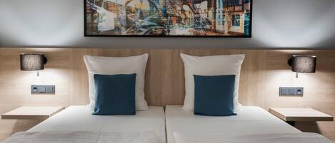 A double bed with white and blue pillows, a wooden headboard, and a large abstract painting above.