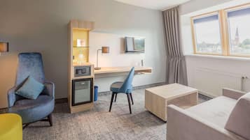 A hotel room with a seating area, a desk, a television, and a window with a view.