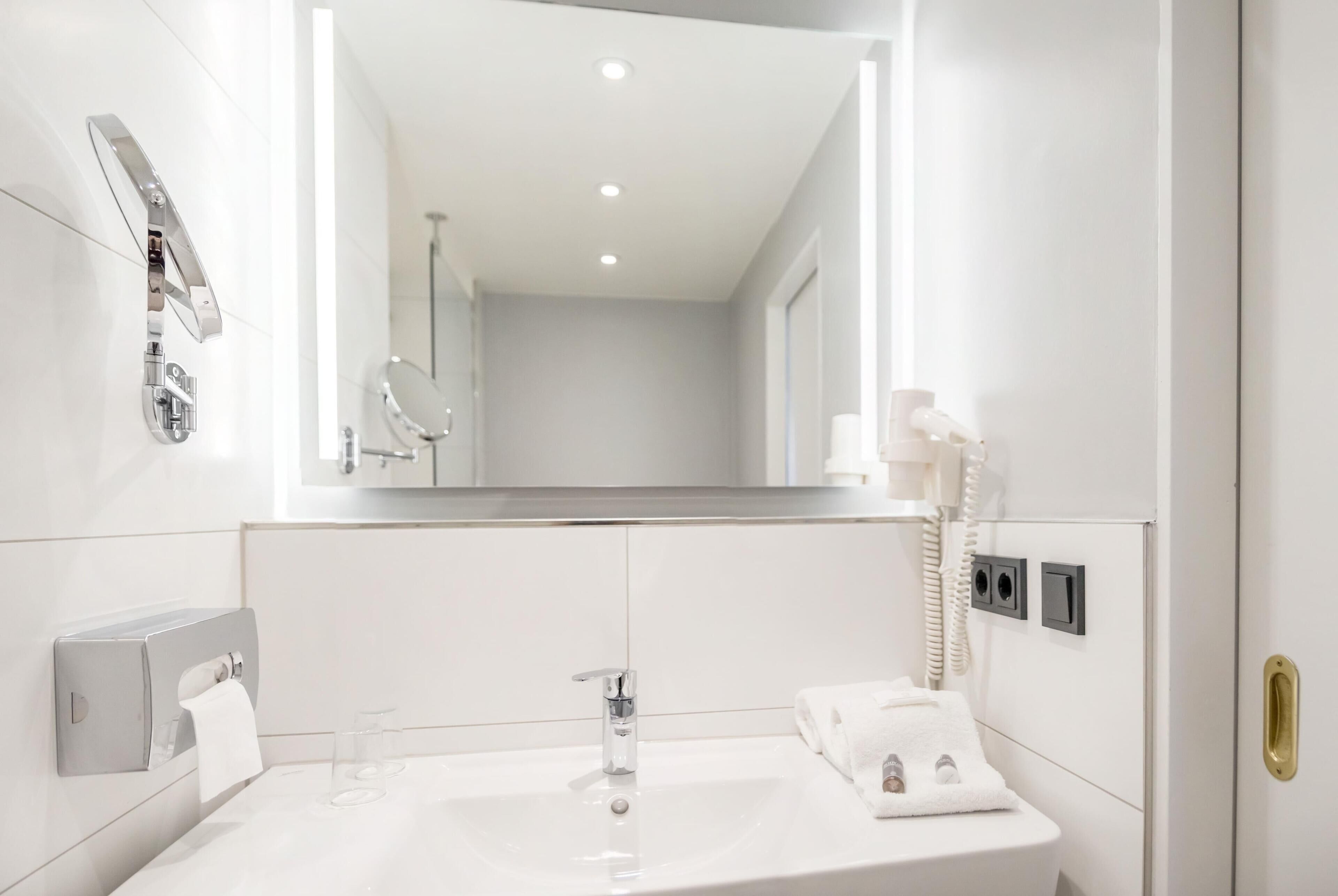 A modern bathroom with a white sink, a mirror, a towel dispenser, and a telephone.