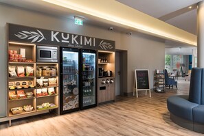 A KUKIMI shop with a microwave, refrigerator, and shelves stocked with snacks and beverages.