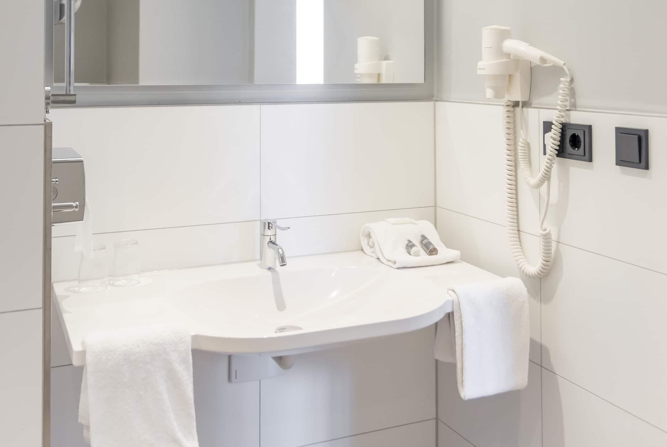A bathroom with a white sink, a mirror, a hairdryer, and a towel rack.