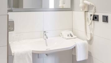 A bathroom with a white sink, a mirror, a hairdryer, and a towel rack.