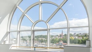 Een modern interieur met grote, rondbogen ramen die uitzicht bieden op een jachthaven en gebouwen.