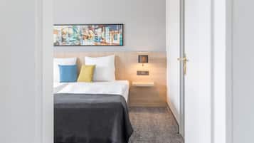 A hotel room with a bed, a nightstand, a wall-mounted lamp, and a framed picture above the bed.