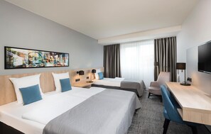 A hotel room with two beds, a desk, a chair, a TV, and a large abstract painting on the wall.