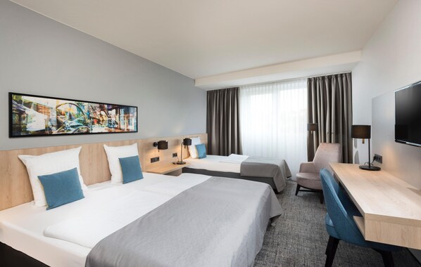 Habitación de hotel con dos camas, un escritorio, una silla, un televisor y un cuadro abstracto grande en la pared.