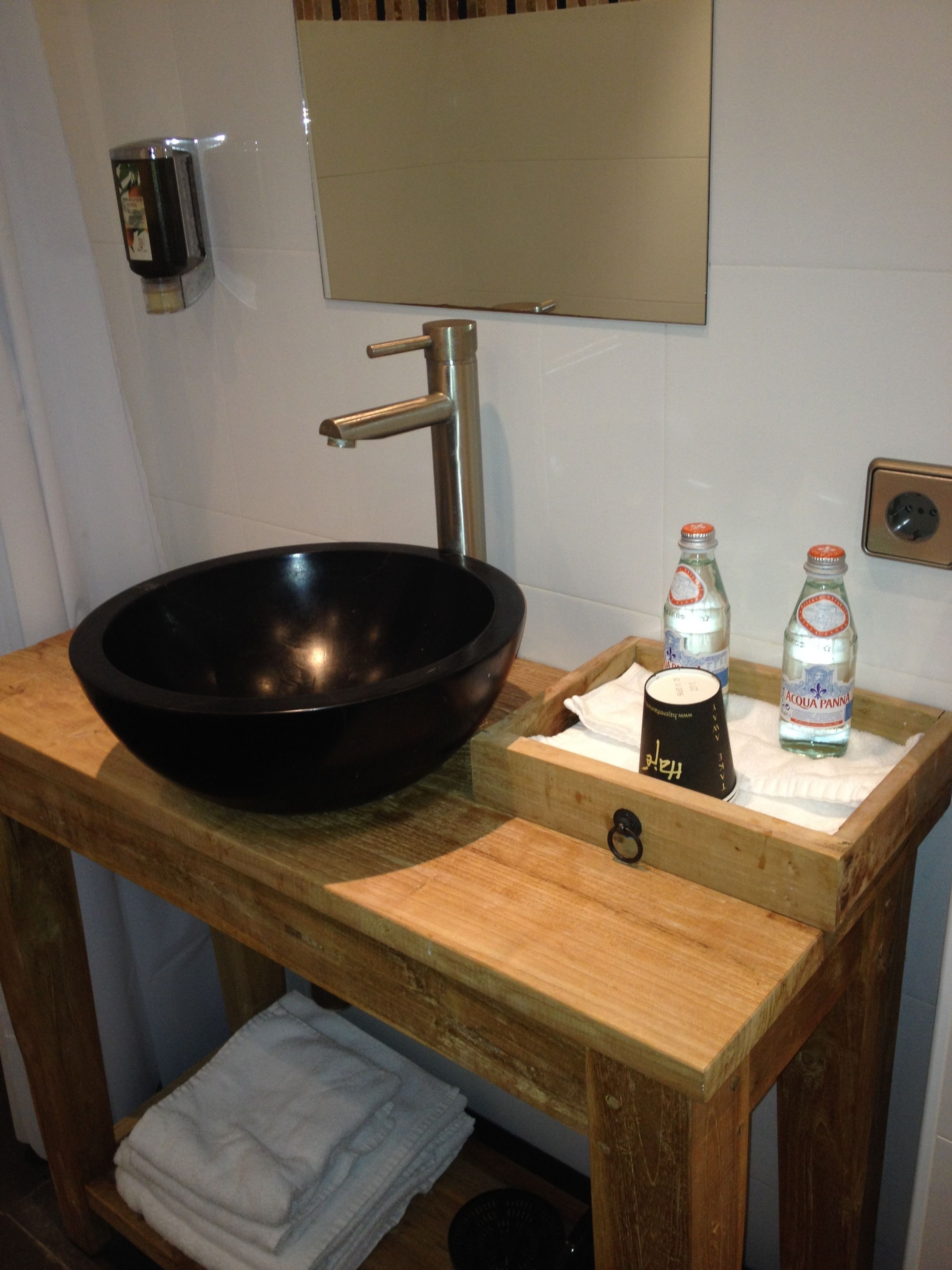 A wooden vanity with a black basin, a mirror, and two bottles of water.