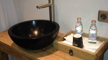 A wooden vanity with a black basin, a mirror, and two bottles of water.