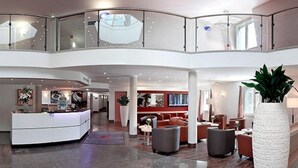 Eine geräumige Lobby mit einer zentralen Rezeption, Sitzbereichen und einer Glasumlaufung, die den unteren Bereich überblickt.