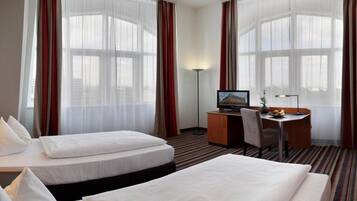 Quarto de hotel com duas camas, uma mesa, uma televisão e um abajur.