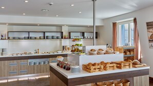 Eine moderne Frühstückstheke mit verschiedenen Speisen und Getränken, Holzschränken und einem großen Fenster mit Vorhängen.