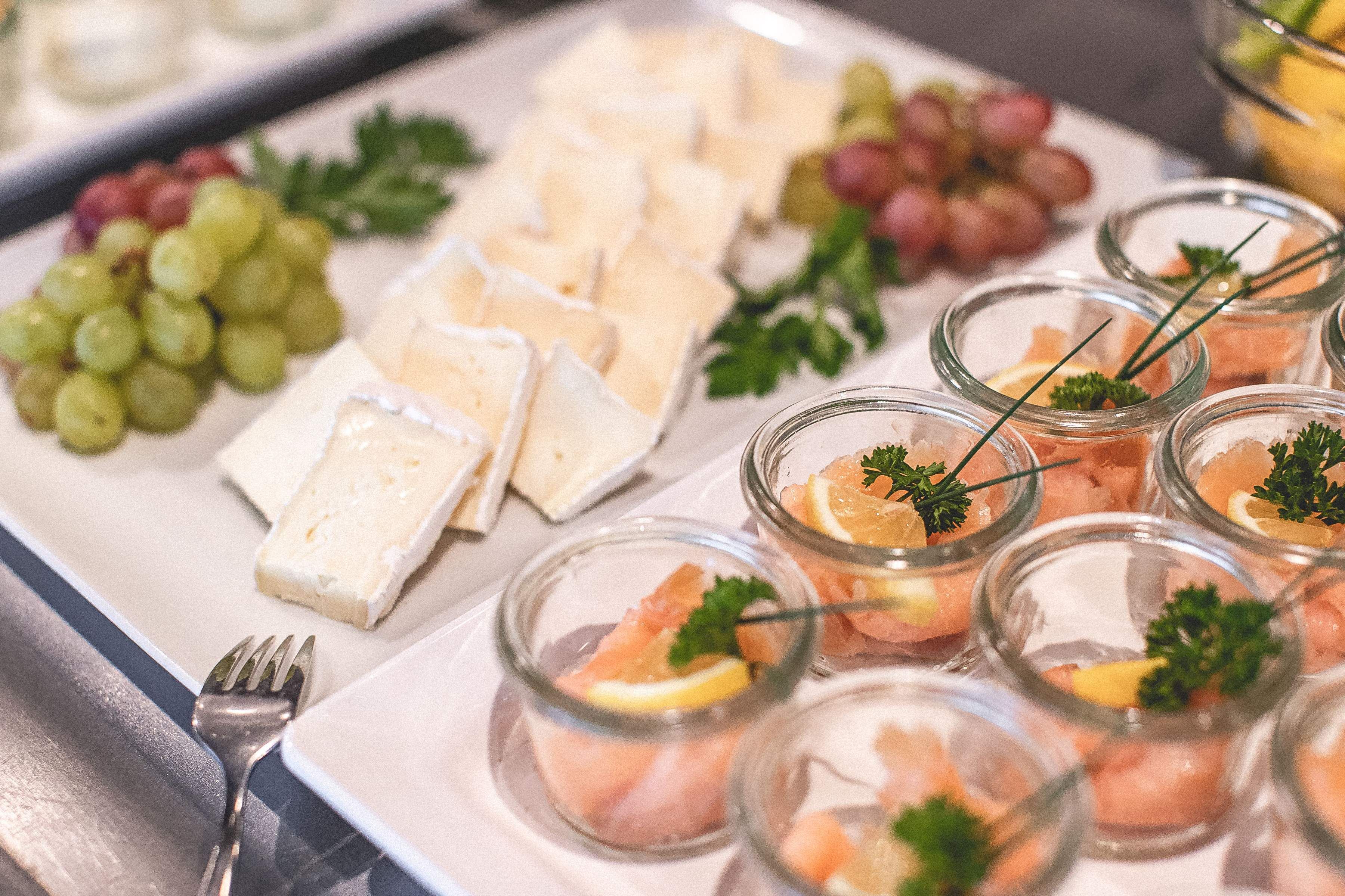 A buffet with various food items including cheese, grapes, and salmon garnished with parsley.