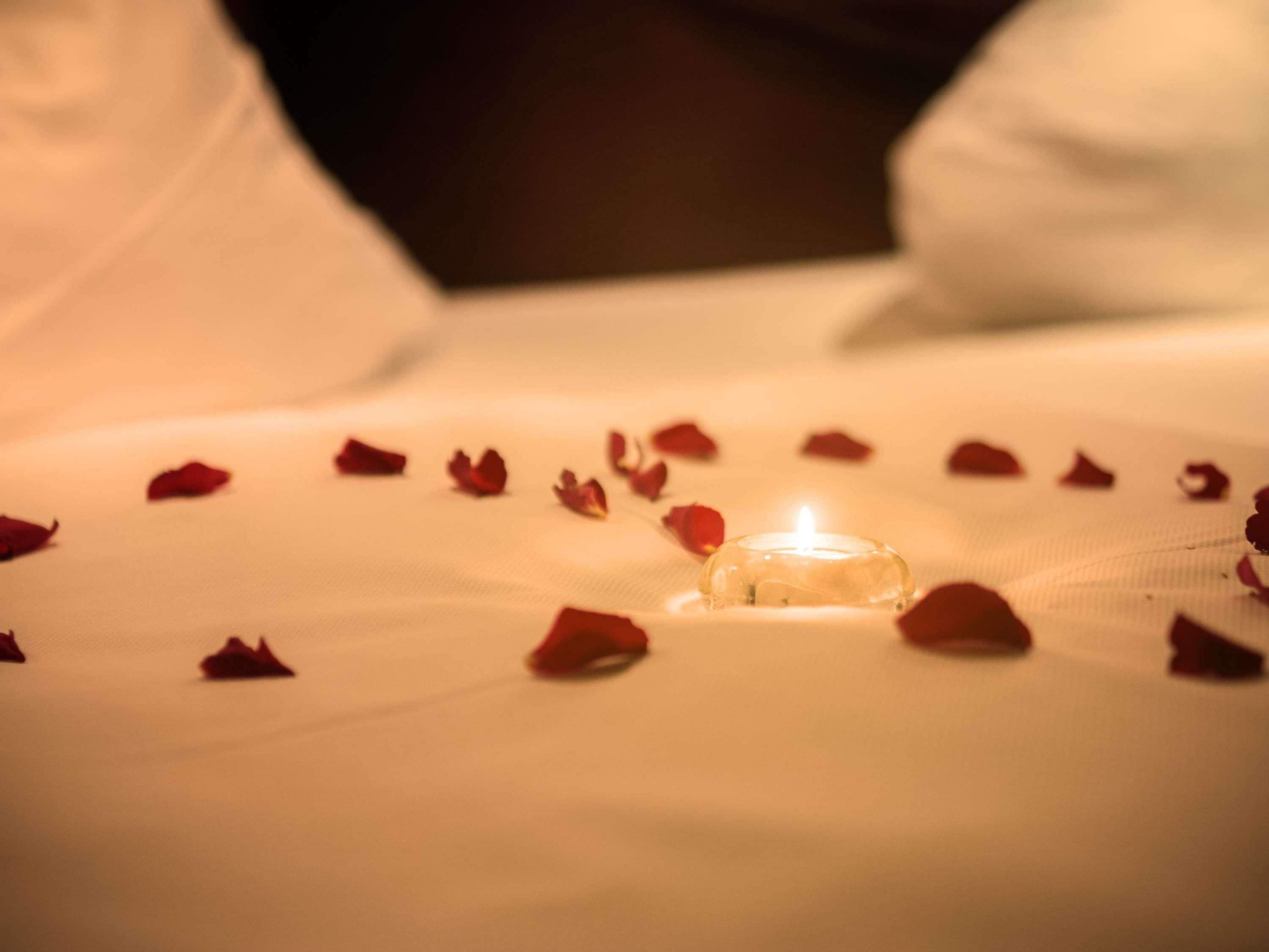 Un lit avec une bougie allumée et des pétales de rose éparpillés.