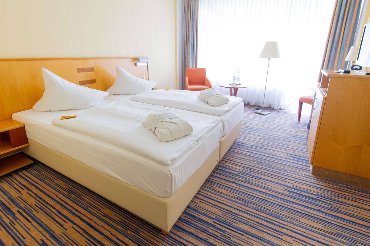 Ein Hotelzimmer mit zwei Betten, einem Schreibtisch, einem Stuhl und einer Lampe.
