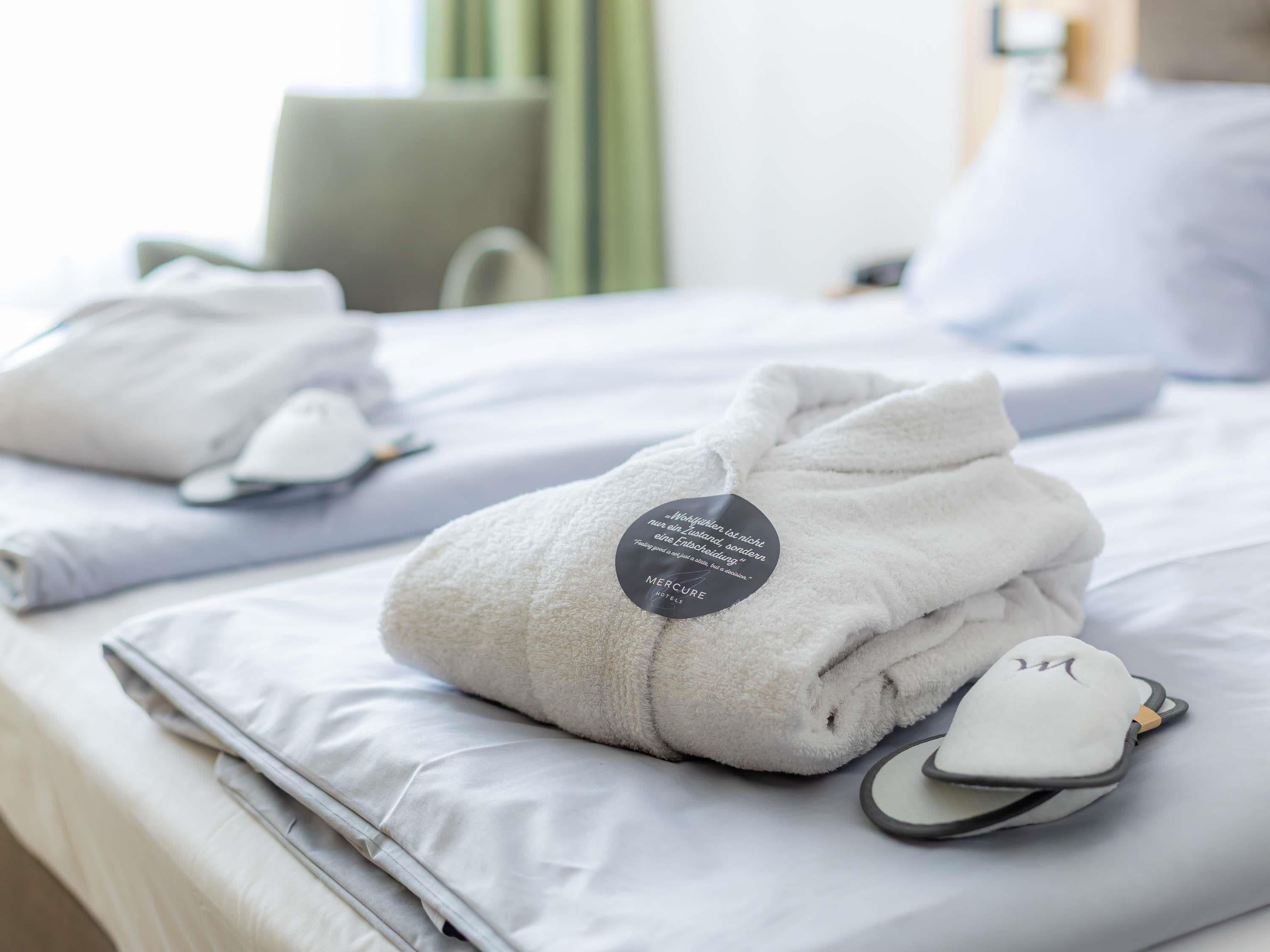 A hotel room with neatly folded towels, a pair of slippers, and a pillow with a tag.