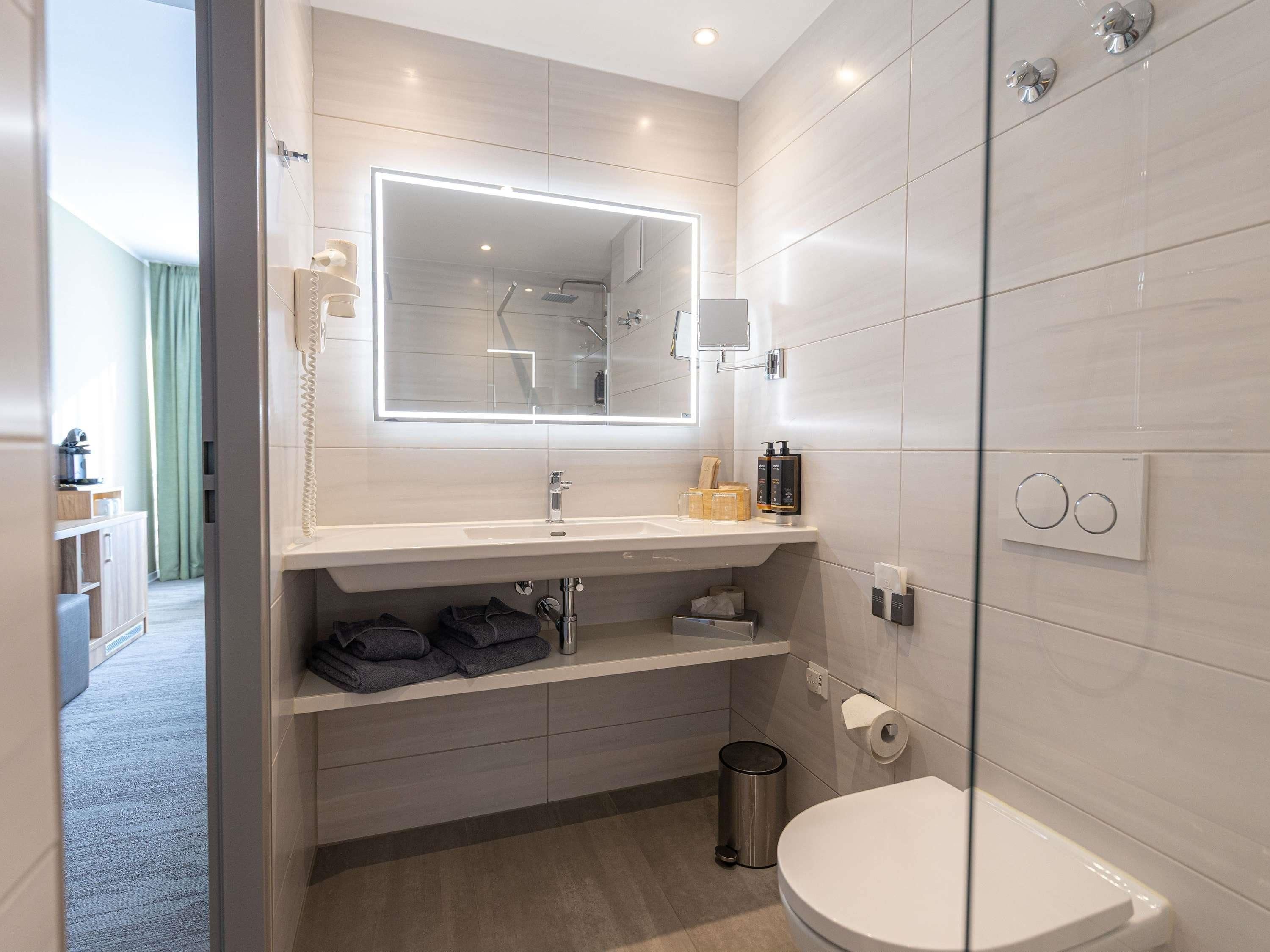 Un baño moderno con cabina de ducha de vidrio, un espejo grande, un lavabo blanco y un inodoro.