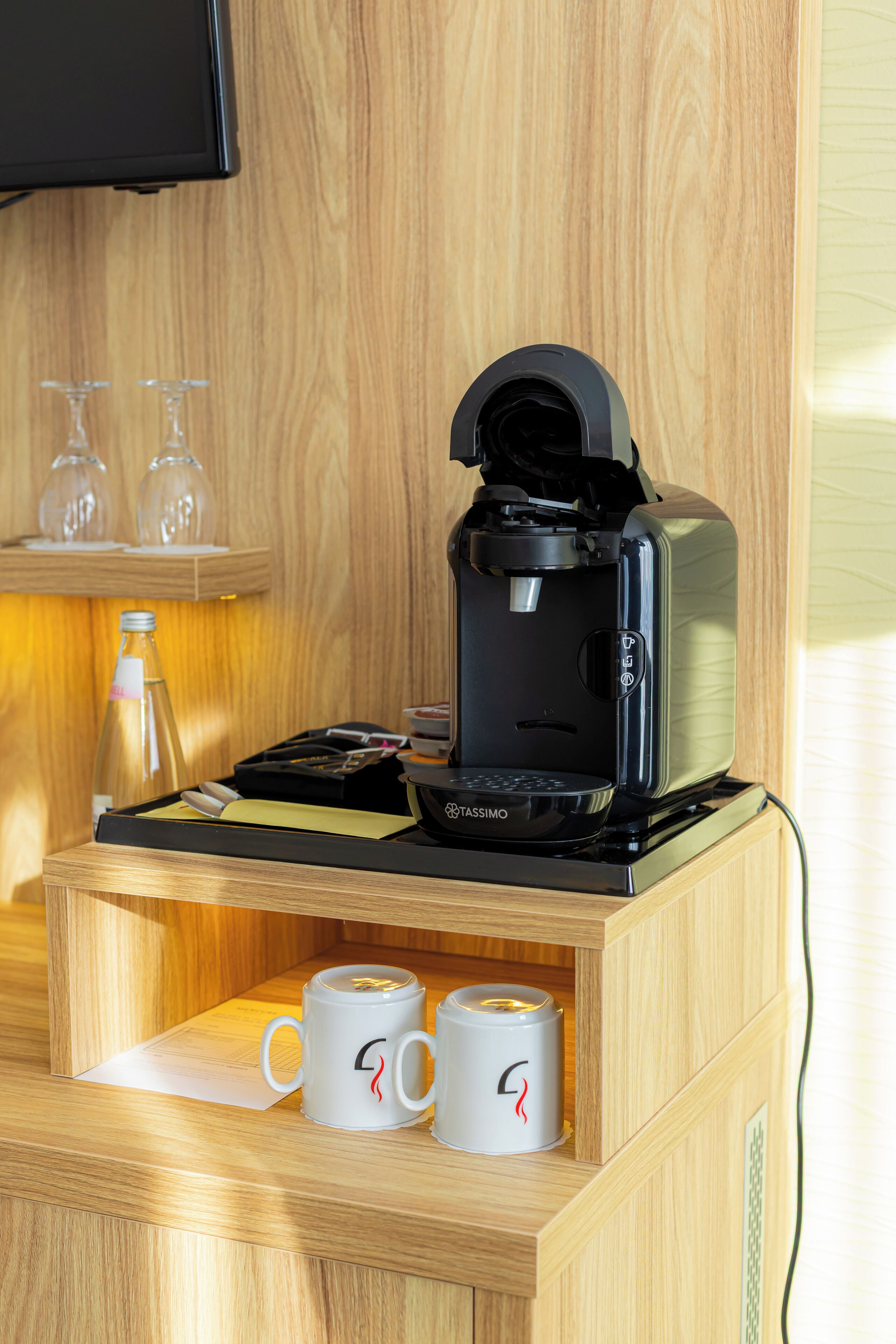 Eine Kaffeemaschine auf einer Holzauslage, dazu zwei weiße Tassen und eine Glasflasche.