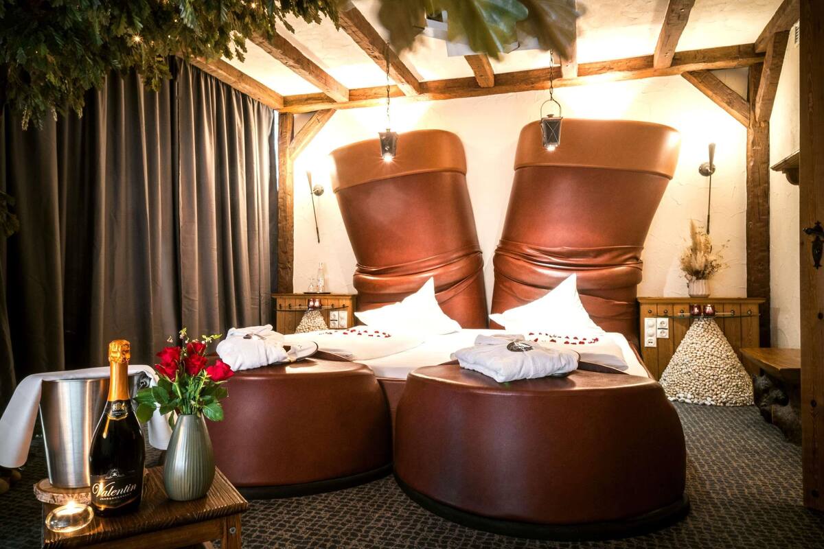 Ein Zimmer mit einem großen Bett, einem Nachttisch mit Flasche und Blumen sowie einer hängenden Pflanze.