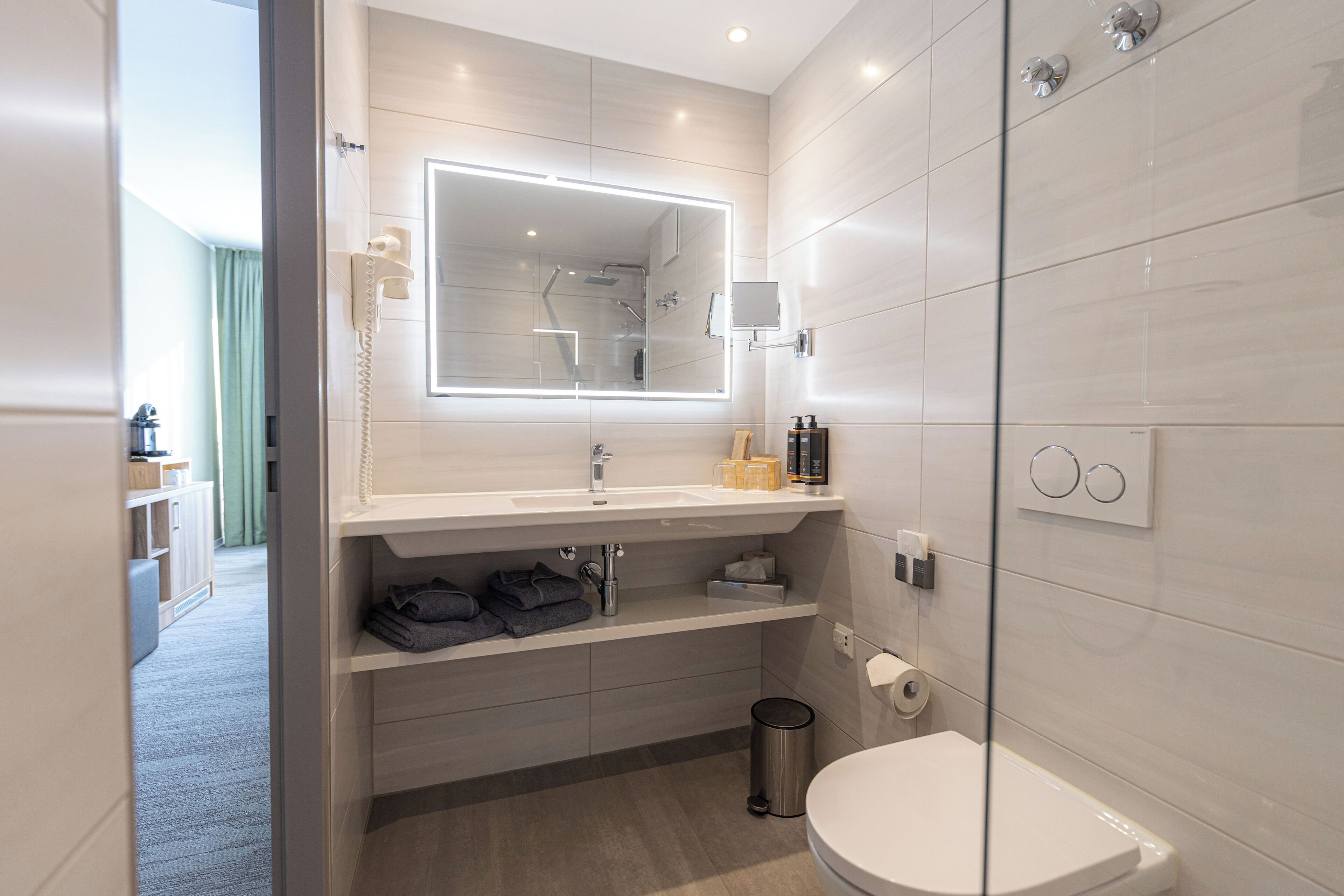 Un baño moderno con cabina de ducha de vidrio, un espejo grande, un lavabo blanco y un inodoro.
