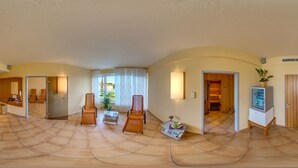 A spacious living area with a tiled floor, a seating area with chairs, a small table with a tray, and a television on a stand. - Mercure Hotel Riesa Dresden Elbland (Riesa)