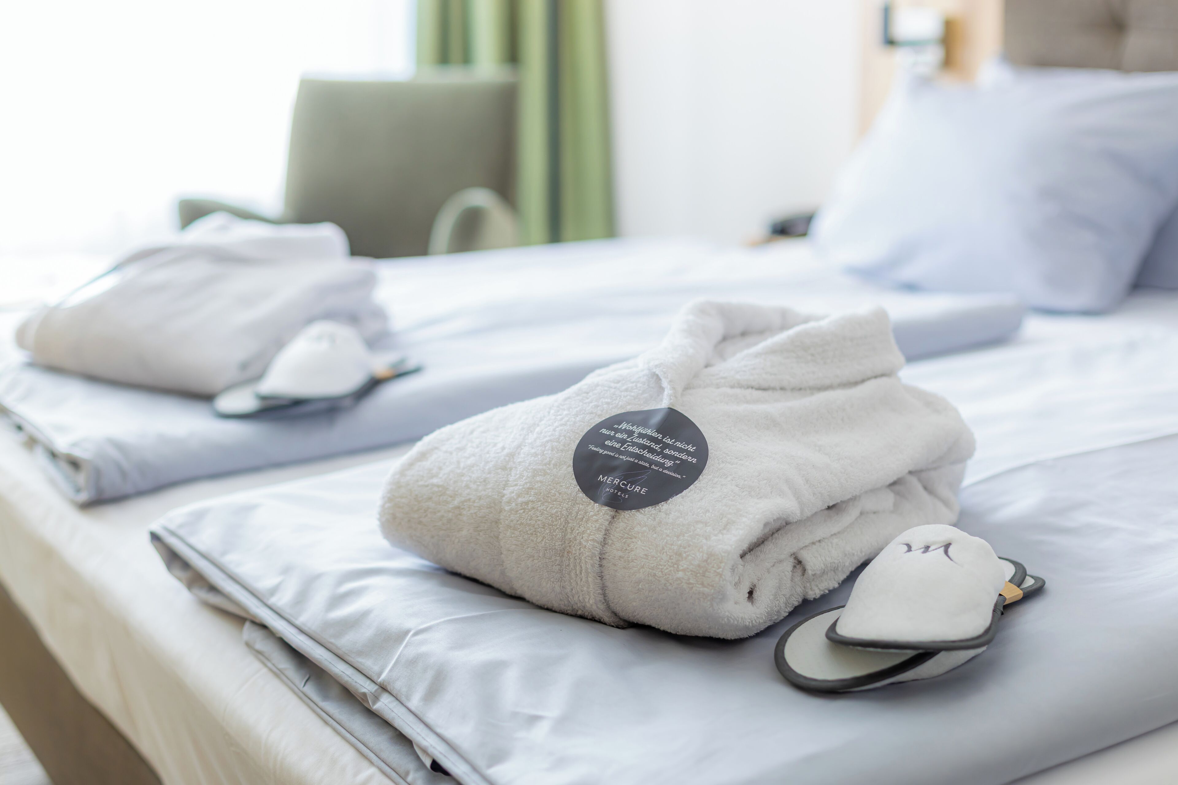 A neatly made bed with folded towels and slippers, a pillow, and a tag indicating a brand.