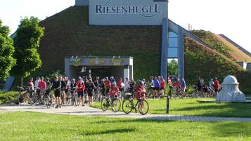 A group of cyclists at a cycling event near a building with a sign reading "Riesenhugel".