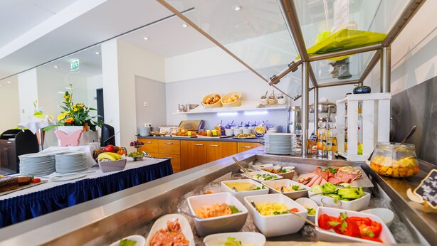 A buffet with various food items and a seating area with a table and chairs. - Mercure Hotel Riesa Dresden Elbland (Riesa)