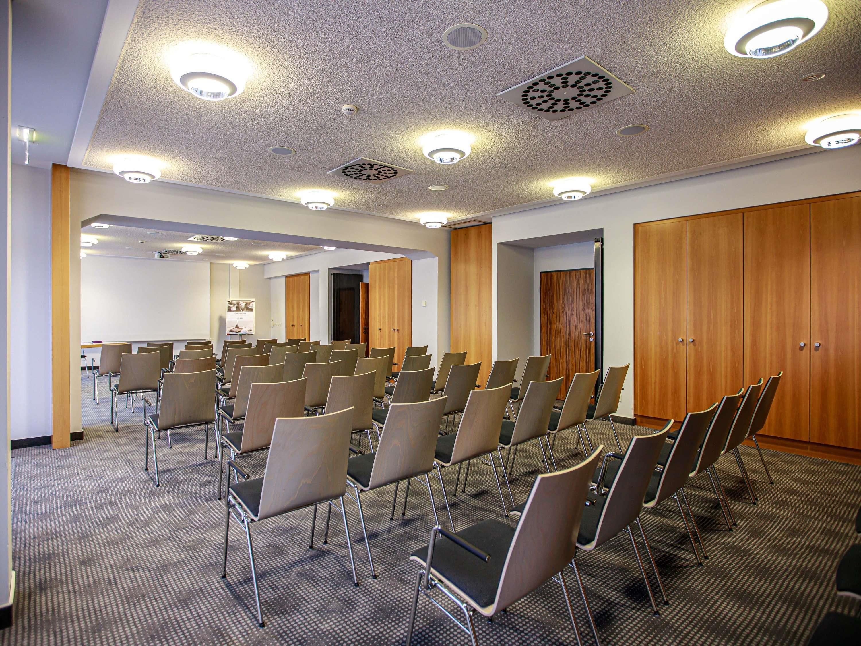 A conference room with rows of chairs, wooden wardrobes, and ceiling lights.