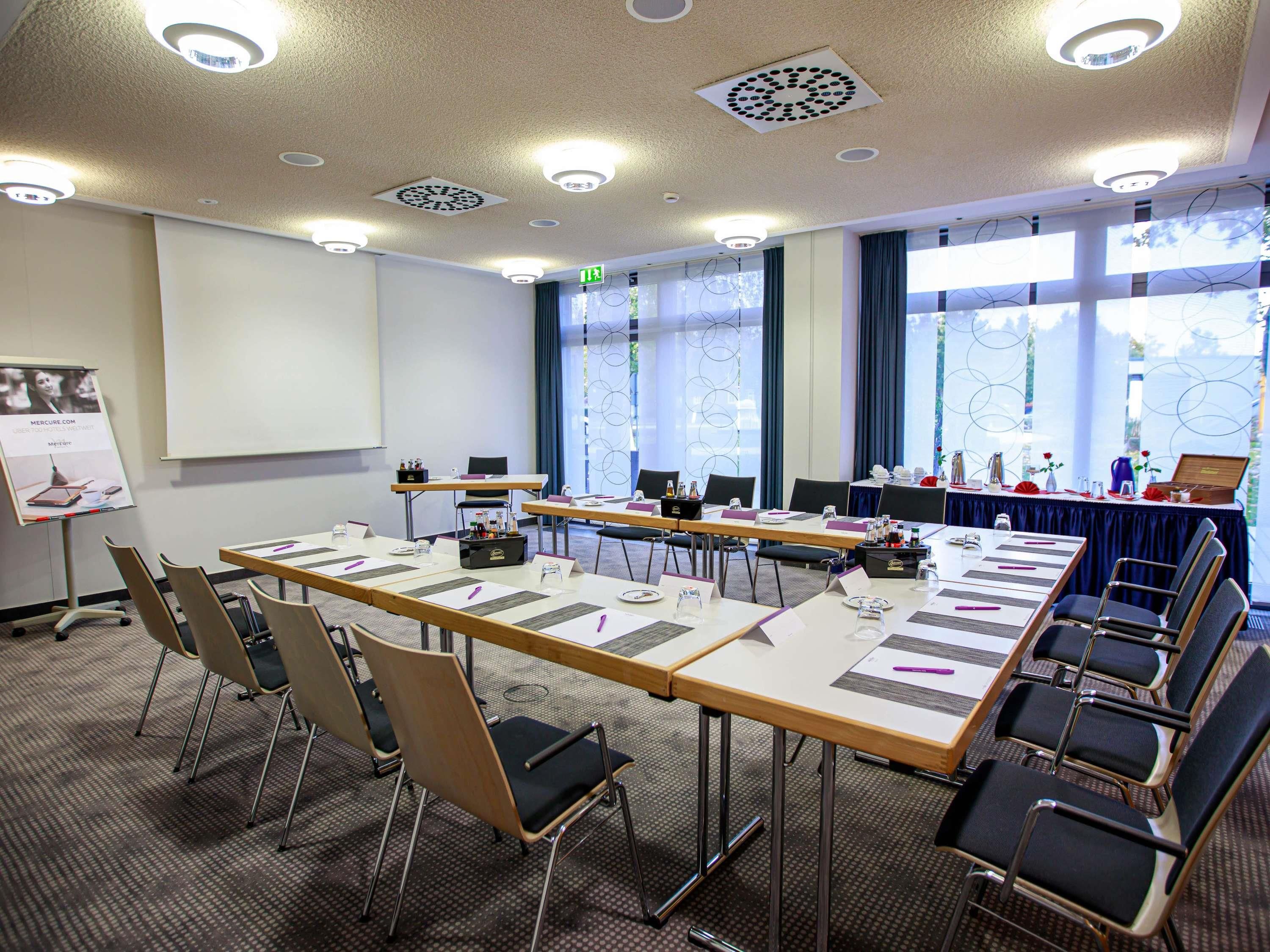A conference room with a long table, chairs, a projector screen, and a presentation board.