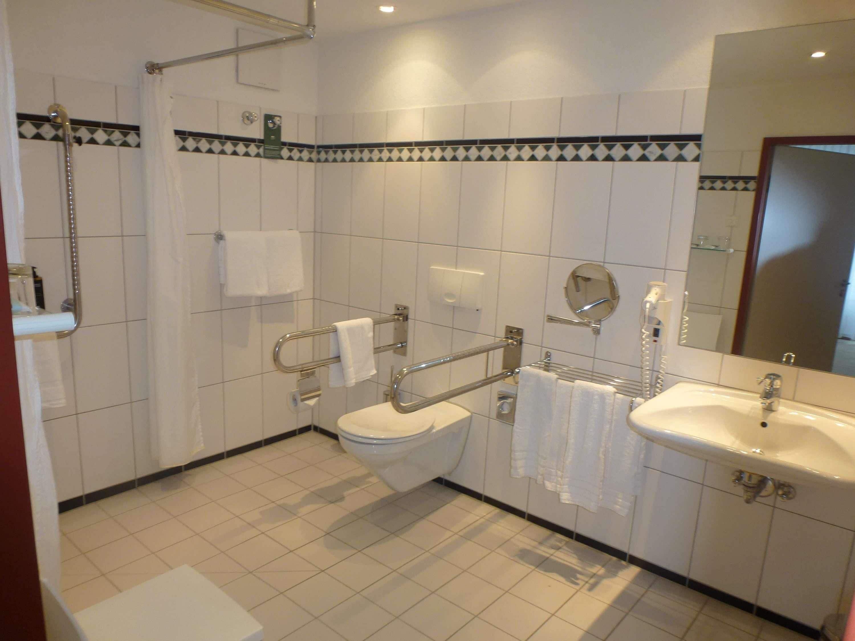 Un baño con inodoro, lavamanos y barras de apoyo.