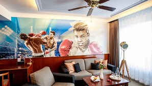 A hotel room with a large sports-themed mural, a ceiling fan, a sofa, a coffee table, and a desk with a lamp.