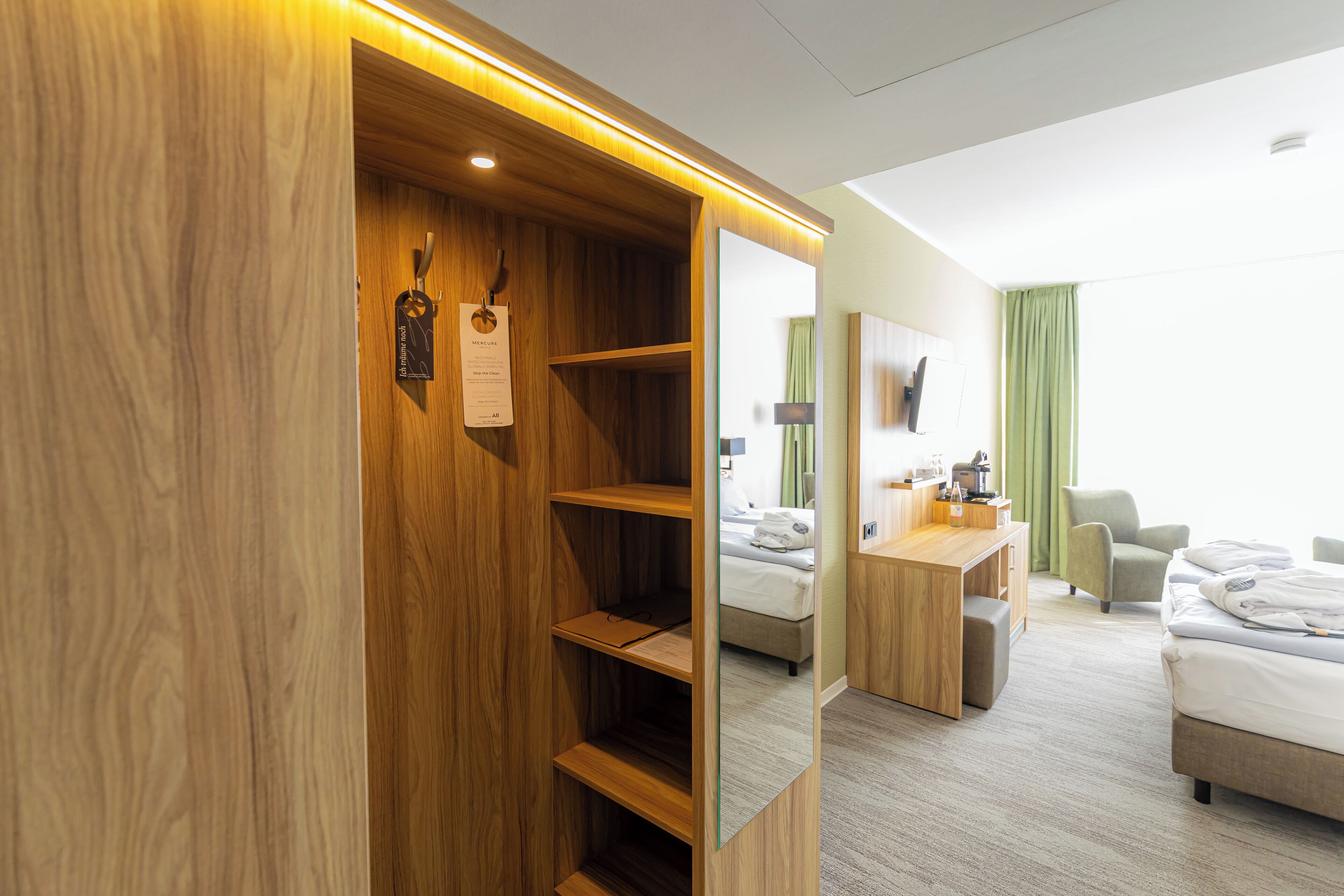 Habitación de hotel con un armario de madera, un escritorio con silla, una cama y un espejo que refleja la habitación.